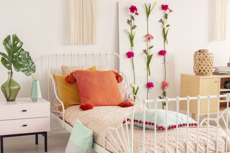 White metal bed with colorful pillows and doted bedding in chic boho bedroom interior