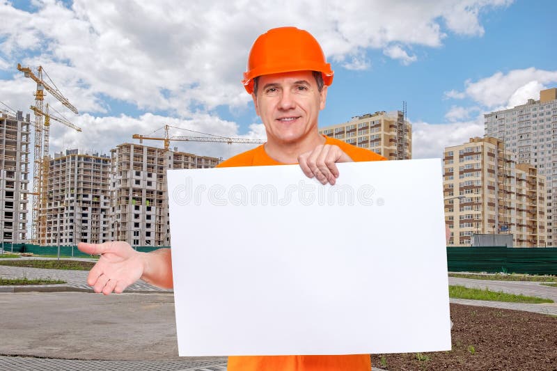 White smiling middle-aged handsome worker wearing orange hard hat, holding blank paper sheet in hand stock photography White smiling middle-aged handsome worker wearing orange hard hat, holding blank paper sheet in hand stock photography