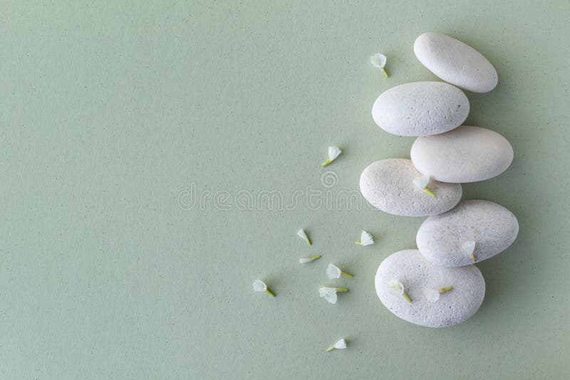 White stones stack and flowers on green background. Card for meditation, spa concept. Top view and flat lay stock photography