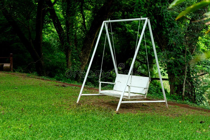 white swing bench chair under green tree