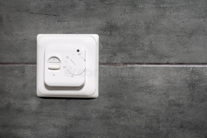 White switch and underfloor heating thermostat on a gray concrete wall in a modern bathroom royalty free stock photo