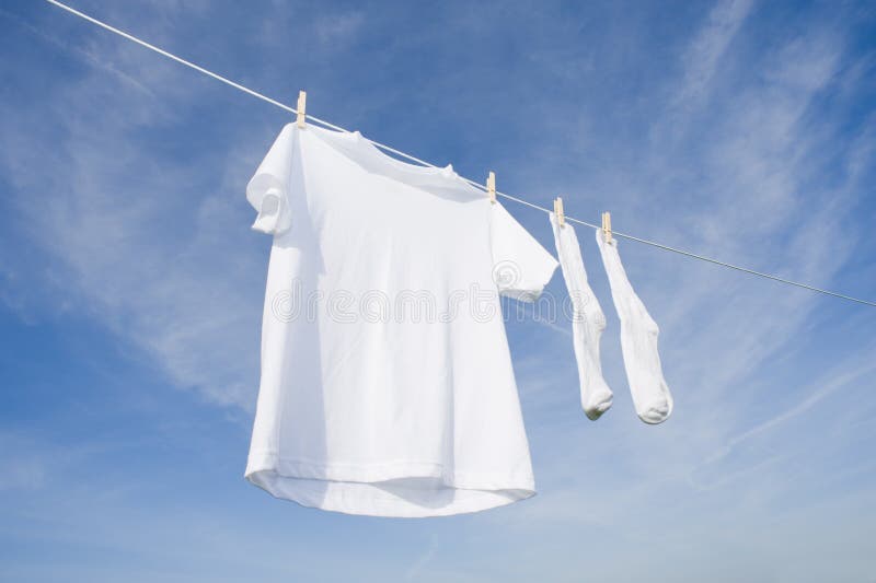 Un bianco t-shirt appeso a una corda da bucato davanti a un cielo blu di sfondo con copia di spazio.