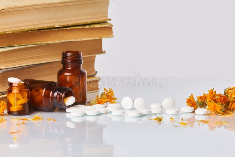White tablets and pills with marigold Calendula and old books on white mirror background. royalty free stock photo White tablets and pills with marigold Calendula and old books on white mirror background. royalty free stock photo
