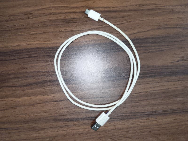 White USB data transfer charging cable coiled on a wooden surface. One end features a standard USB-A connector, while the other has a smaller connector, possibly Micro-USB or USB-C. The cable is covered in a smooth plastic sheath and is approximately standard length. The wood surface has a distinct brown grain pattern, providing a contrasting background to the bright cable. Usb data transfer stock images, royalty-free photos and pictures