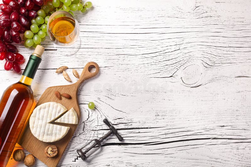 White wine bottle, grape, cheese and wineglass on white wooden board