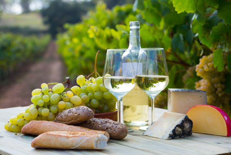 White wine with cheese, bread and grapes in vineyard