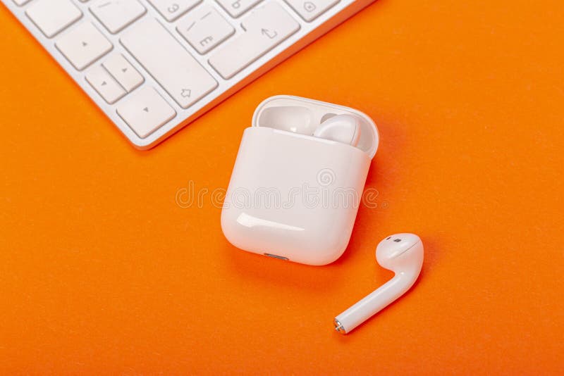 White wireless earphones with charging case on bright orange background