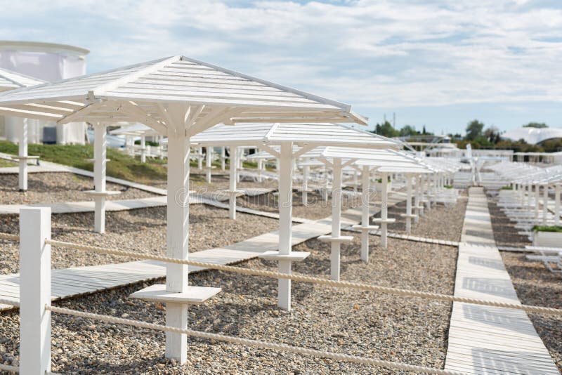 White Wooden Beach Umbrellas, Paths and Deck Chairs on the Seashore