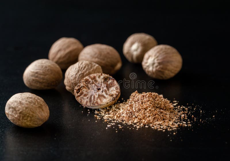 Whole Nutmeg Nuts and Nutmeg Powder in a Black Background Stock Photo