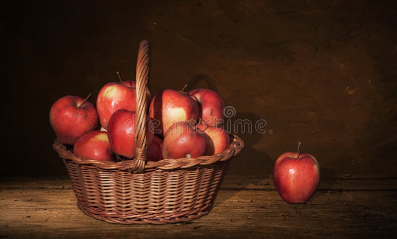 Wicker Basket with apples and one apple on table, dark painting background.