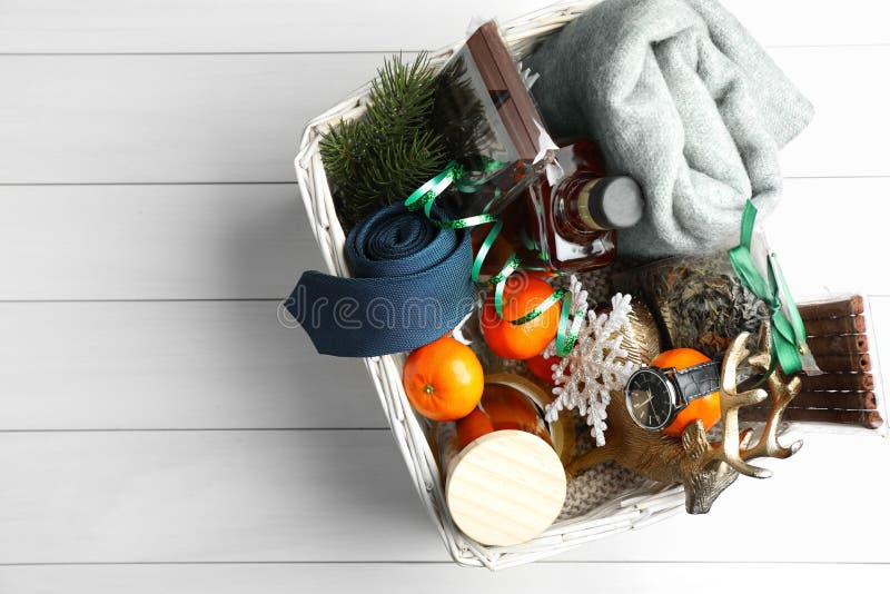 Wicker basket with Christmas gift set on white wooden table, top view. Space for text