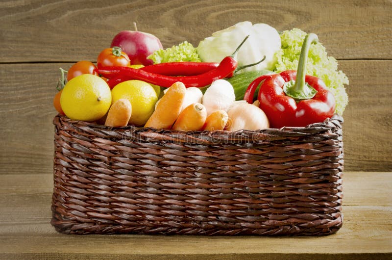 Wicker basket with fruits and vegetables on wooden table