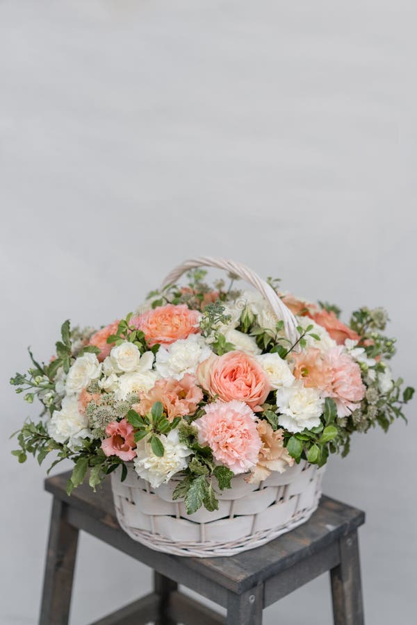 Wicker basket with mix beautiful flowers on wooden table near gray wall. Beautiful garden flowers in the arrangement