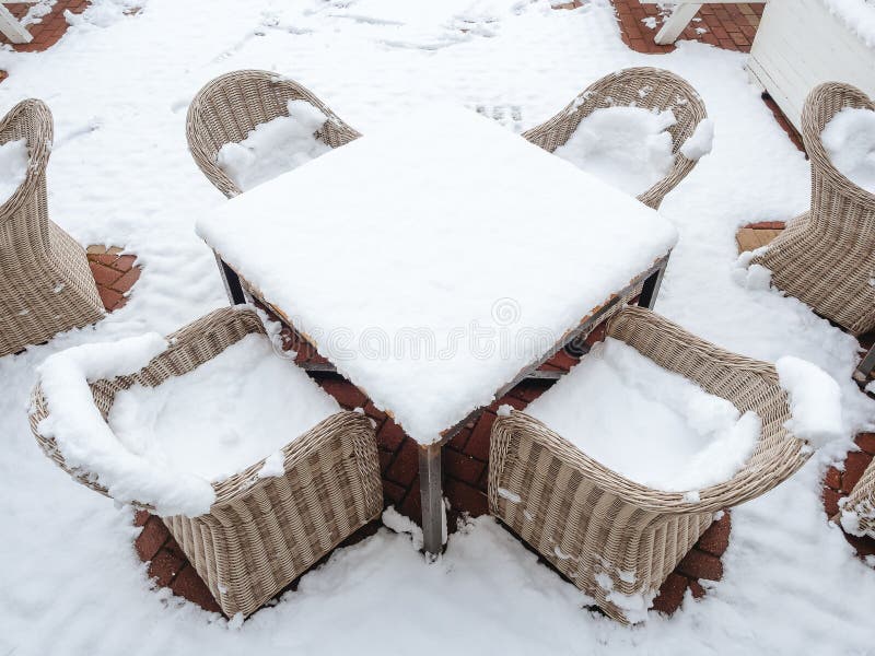 Wicker Chairs Strewn with Snow Stand Around a Snowstrewn Table on a