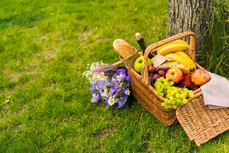 Wicker picnic basket with fruits and wine, cheese, baguette and bouquet of beautiful flowers