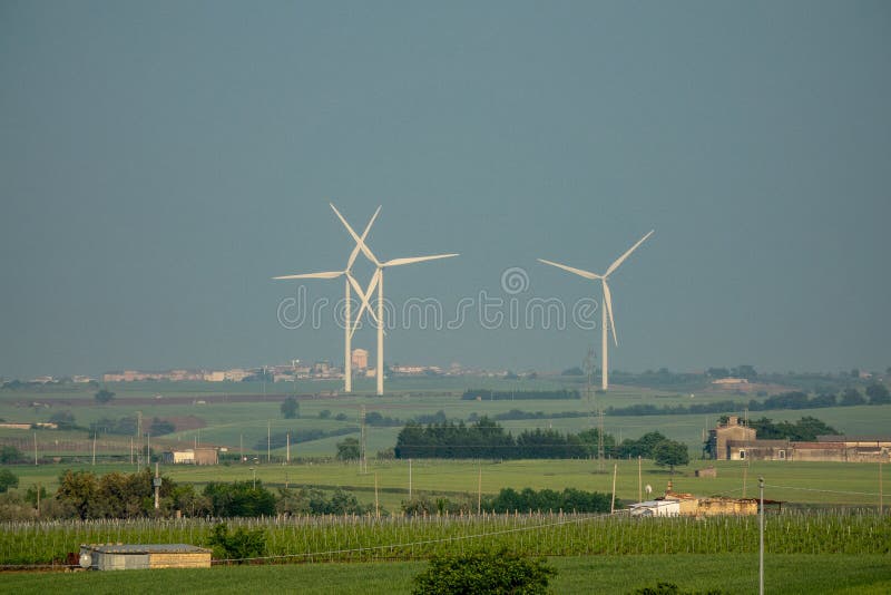 Wide angle shot of three white wind fans on a green field during daytime stock photo