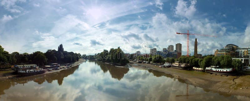 Wide panoramic view of the thames at kew brige with houseboats and surrounding buildings with dramatic clouds