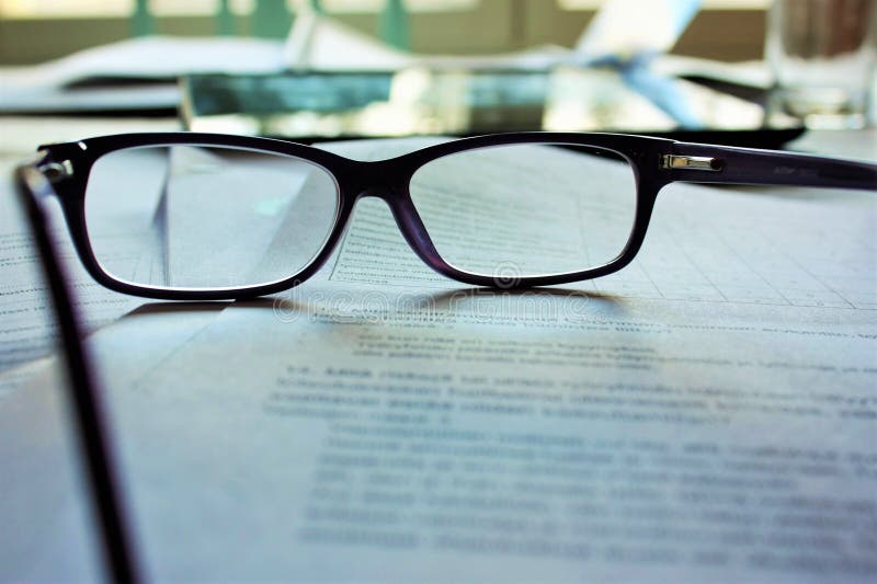 Wide selective closeup shot of black glasses on a pile of papers.