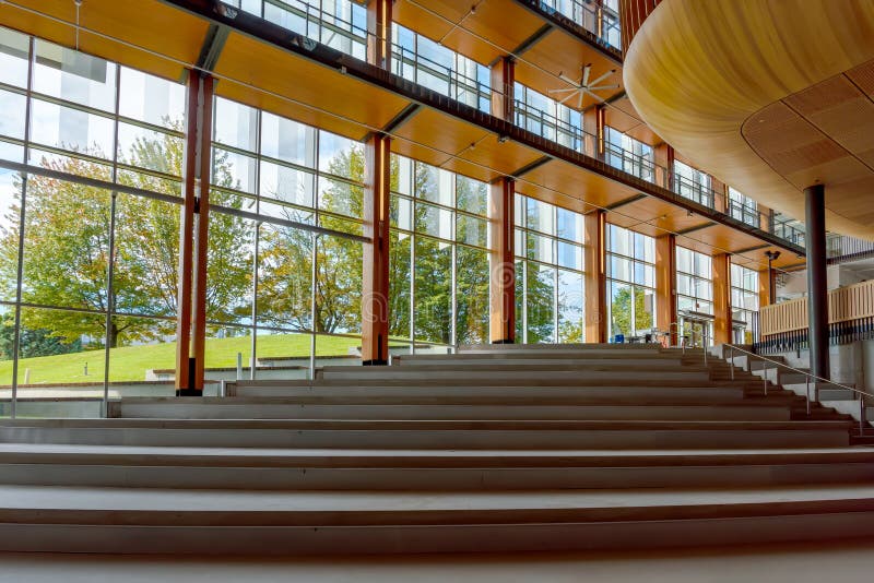 A wide staircase with steps up in the interior of a modern building with wooden columns, large glass windows, green grass, blue sky and trees. A wide staircase with steps up in the interior of a modern building with wooden columns, large glass windows, green grass, blue sky and trees