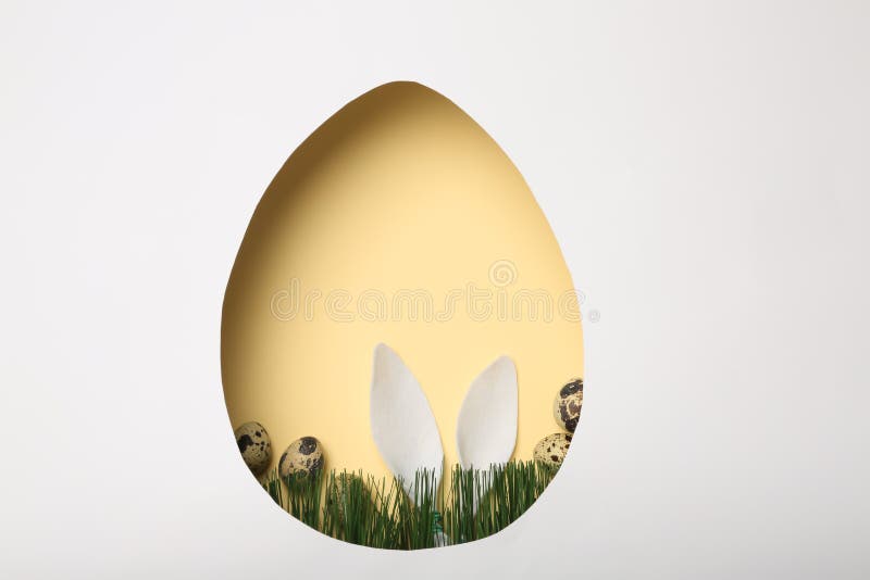 View of composition with Easter bunny ears on color background through egg shaped hole, top view. Space for text. View of composition with Easter bunny ears on color background through egg shaped hole, top view. Space for text