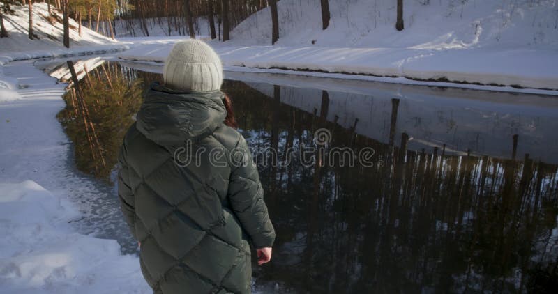 Widok wsteczny kobieta w kurtce rzucająca śnieg w rzece chodząca w parku.