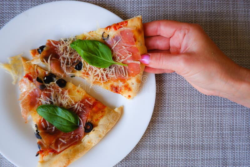 Widok z bliska na kobiecą dłoń zabiera kawałek pizzy z białej płytki. apetyt na pyszną pizzę zdjęcia stock