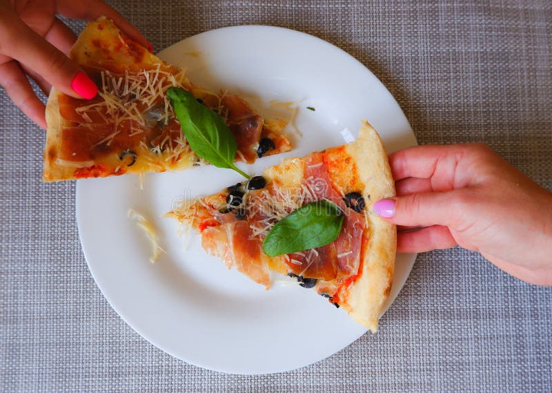 Widok z bliska na kobiecą dłoń zabiera kawałek pizzy z białej płytki. apetyt na pyszną pizzę obraz stock