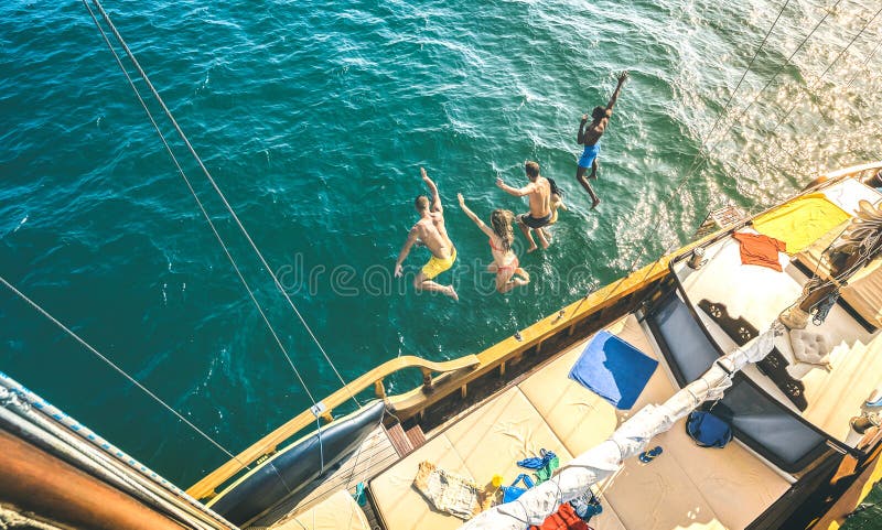 Aerial view of happy millenial friends jumping from sailboat on sea ocean trip - Rich guys and girls having fun together in exclusive boat party day - Luxury vacation concept. Aerial view of happy millenial friends jumping from sailboat on sea ocean trip - Rich guys and girls having fun together in exclusive boat party day - Luxury vacation concept