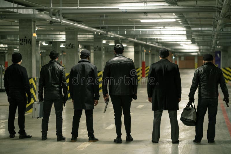 Rear view of row of criminals or gangsters in black standing on parking area while waiting for man with buyout. Rear view of row of criminals or gangsters in black standing on parking area while waiting for man with buyout