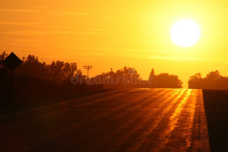 Looking straight into the sunset of a country road with hints of orange and blue in the sky and a silhouetted road with highlights. Looking straight into the sunset of a country road with hints of orange and blue in the sky and a silhouetted road with highlights.