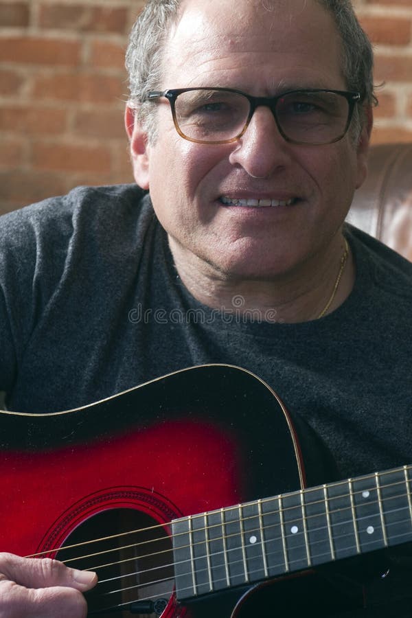 Wieka średniego starszy mężczyzna bawić się gitarę. Wieka średniego starszego mężczyzny muzyk bawić się gitarę akustyczną i wykonuje rozrywkę podczas gdy uśmiechnięty i szczęśliwy