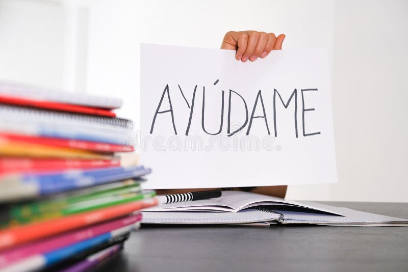 Many books, exercises books on the table and kid hand holding sheet of paper with Spanish word Auydame - Help me - Learning difficulties, school, education concept. Many books, exercises books on the table and kid hand holding sheet of paper with Spanish word Auydame - Help me - Learning difficulties, school, education concept.