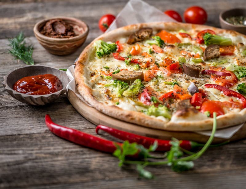 Large vegeterian pizza with sauces and pepper on the side, served on board. Large vegeterian pizza with sauces and pepper on the side, served on board