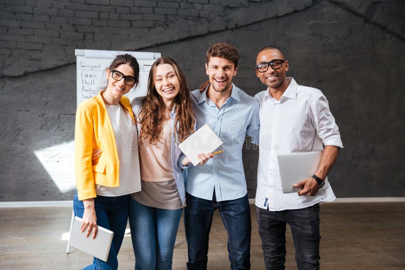 Multiethnic group of happy young business people holding tablet and laptop standing in office. Multiethnic group of happy young business people holding tablet and laptop standing in office