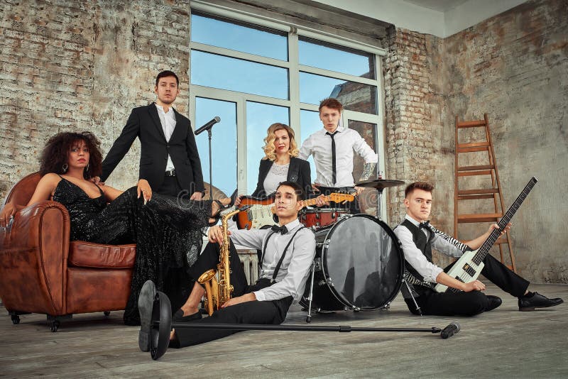 Multi ethnic jazz band posing on a leather sofa against the window in loft. Bass guitar player, electric guitar player, saxophonist and drummer at loft. Jazz music and jam session concept. passion for music and youth culture concepts. Multi ethnic jazz band posing on a leather sofa against the window in loft. Bass guitar player, electric guitar player, saxophonist and drummer at loft. Jazz music and jam session concept. passion for music and youth culture concepts.