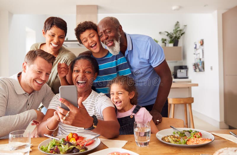 Wielopokoleniowa Mieszana Rodzina Wyścigu Dająca Selfie, Gdy Jadają Jedzenie Wokół Stołu W Domu Razem