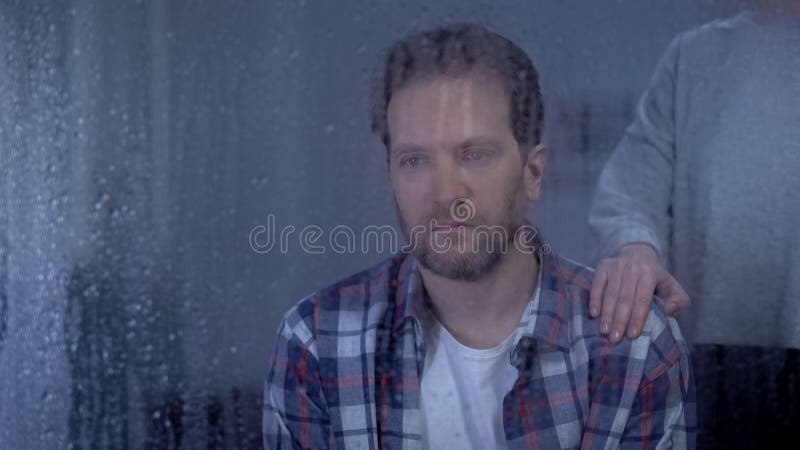 Wife holding hand on shoulder of depressed husband, family support, rainy day