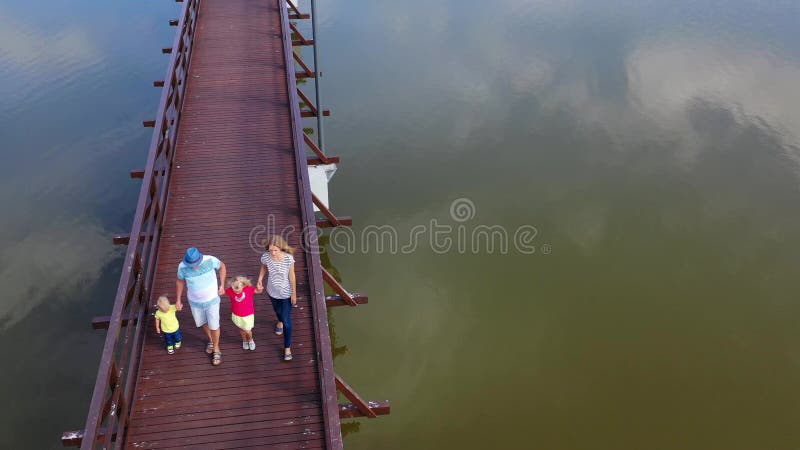Wife with husband and their little kids walking on wooden bridge holding hands