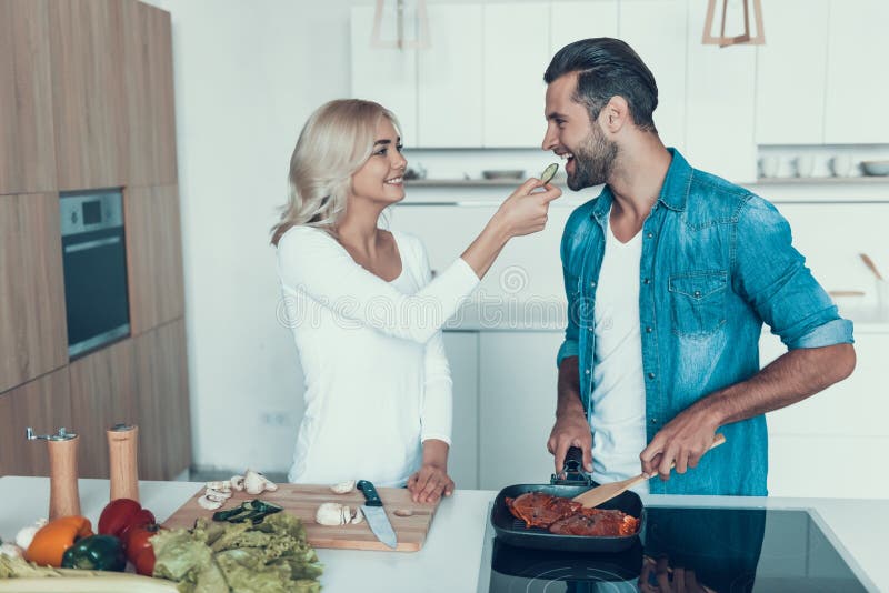 The wife makes salad, while husband fries meat in kitchen.