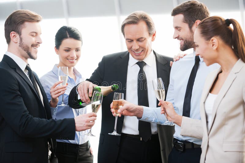 Group of happy business people holding flutes with champagne and smiling while standing close to each other indoors. Group of happy business people holding flutes with champagne and smiling while standing close to each other indoors