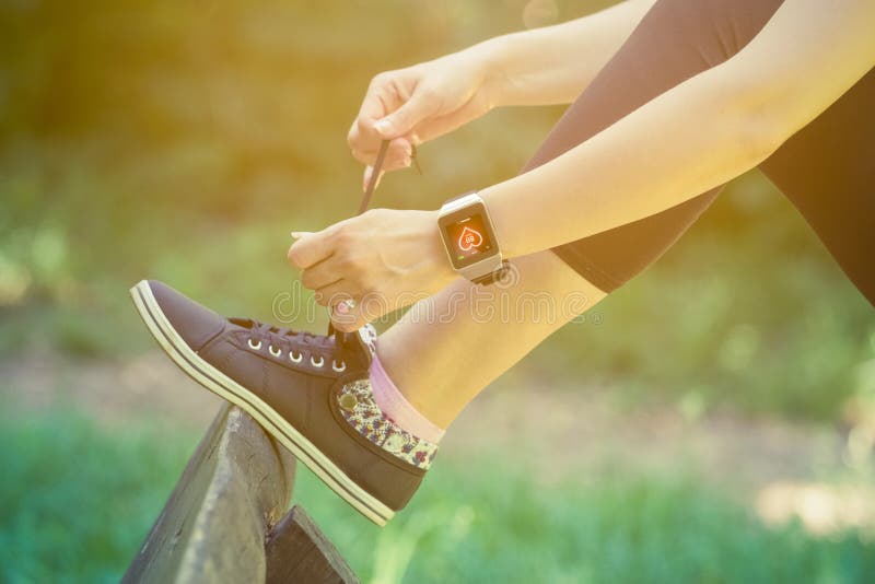Wijfje die slim horloge dragen en schoenveters in het park binden royalty-vrije stock afbeeldingen Wijfje die slim horloge dragen en schoenveters in het park binden royalty-vrije stock afbeeldingen