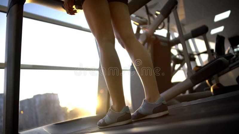 Wijfje die zich op tredmolenmachine bevinden in gymnastiek en van zonsopgang genieten vóór training stock afbeeldingen Wijfje die zich op tredmolenmachine bevinden in gymnastiek en van zonsopgang genieten vóór training stock afbeeldingen