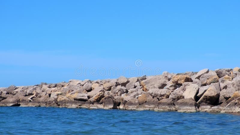 Nature background seascape wild seashore with stones, blue sky water sunny day.