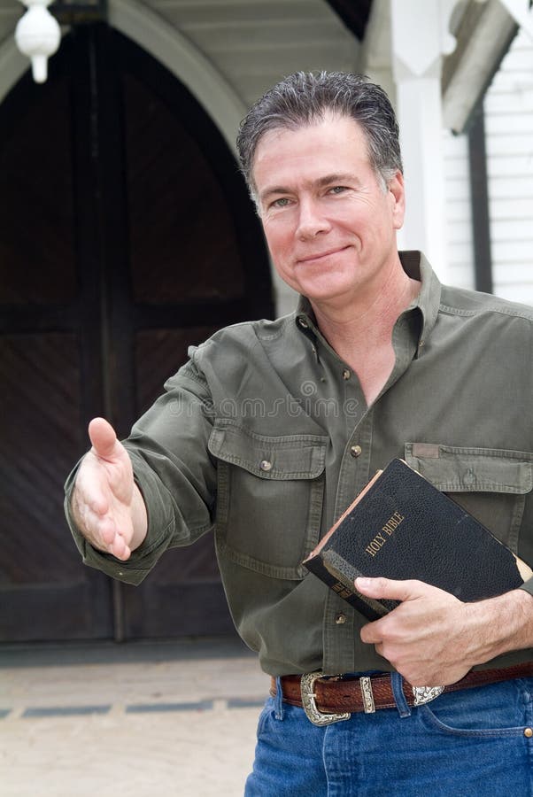 A man standing in front of a church holding a bible with his hand extended as if greeting someone. A man standing in front of a church holding a bible with his hand extended as if greeting someone.