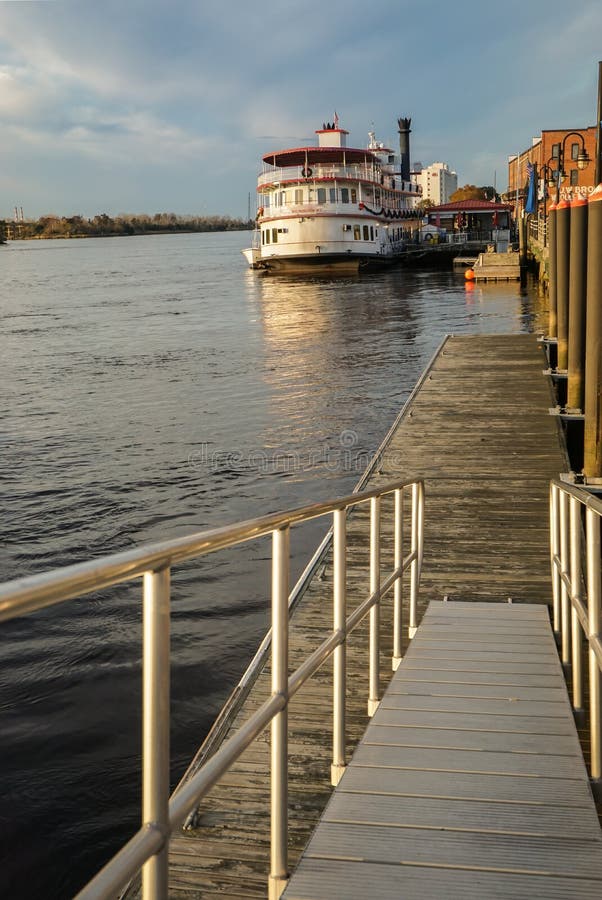 Wilmington NC waterfront and river walk, Cape Fear river. Wilmington boardwalk and ramp in soft evening light with steamboat replica in background on the Cape royalty free stock photography Wilmington NC waterfront and river walk, Cape Fear river. Wilmington boardwalk and ramp in soft evening light with steamboat replica in background on the Cape royalty free stock photography
