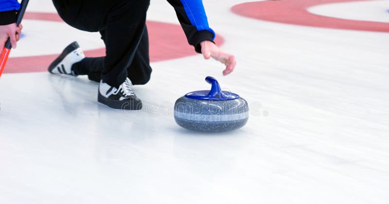 Curling player delivering a stone on a curling rink, sliding over the ice. Curling player delivering a stone on a curling rink, sliding over the ice