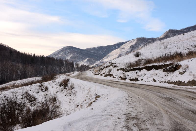 A winding gravel road skirts the slope of a high snow-covered mountain lying in a beautiful valley in winter