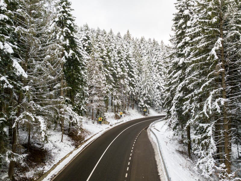 Winding road through the forest, from high mountain pass, winter. Aerial view by drone