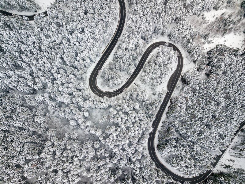 Winding road through the forest, from high mountain pass, winter. Aerial view by drone