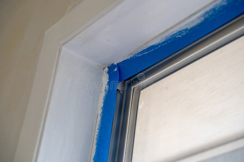 Window trim covered with blue painters tape during home renovation improvements during painting